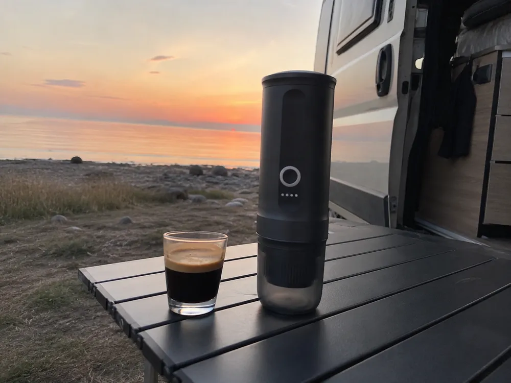Macchina espresso portatile sul tavolino fuori dal camper con il mare all'alba