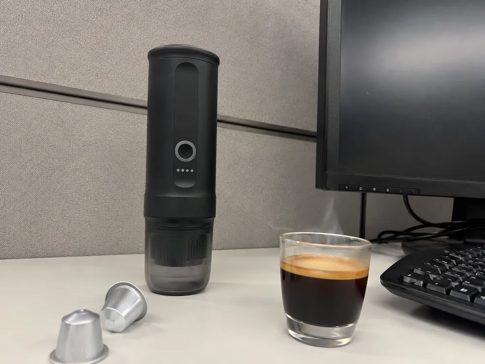 Macchina espresso portatile sulla scrivania in ufficio con le capsule accanto