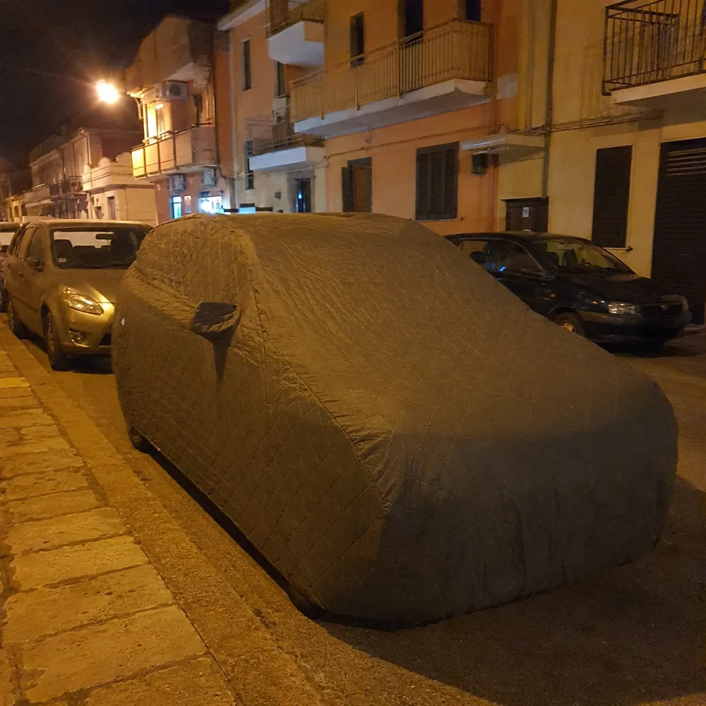 Auto coperta dal telo parcheggiata in strada di sera